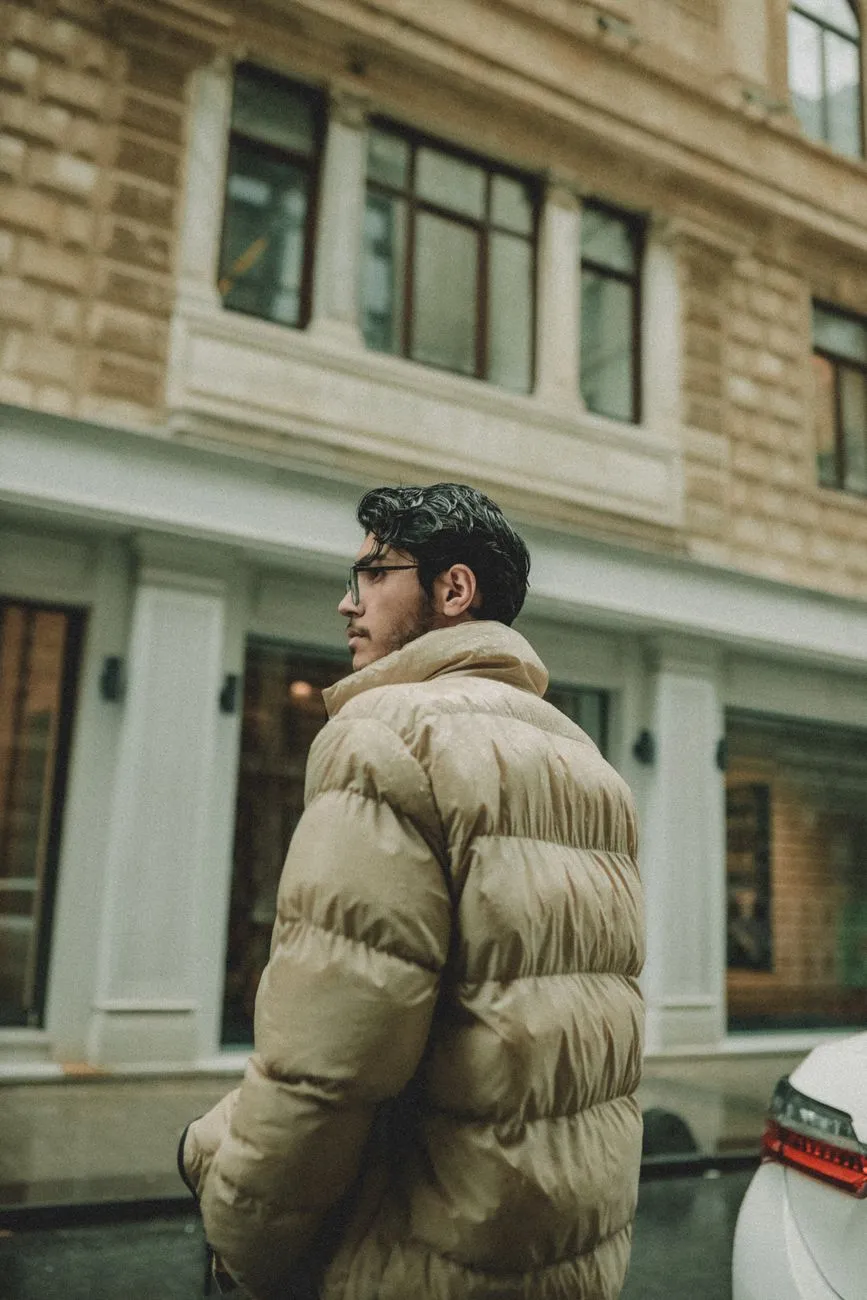Young man with glasses in a beige puffer jacket walking down a city street