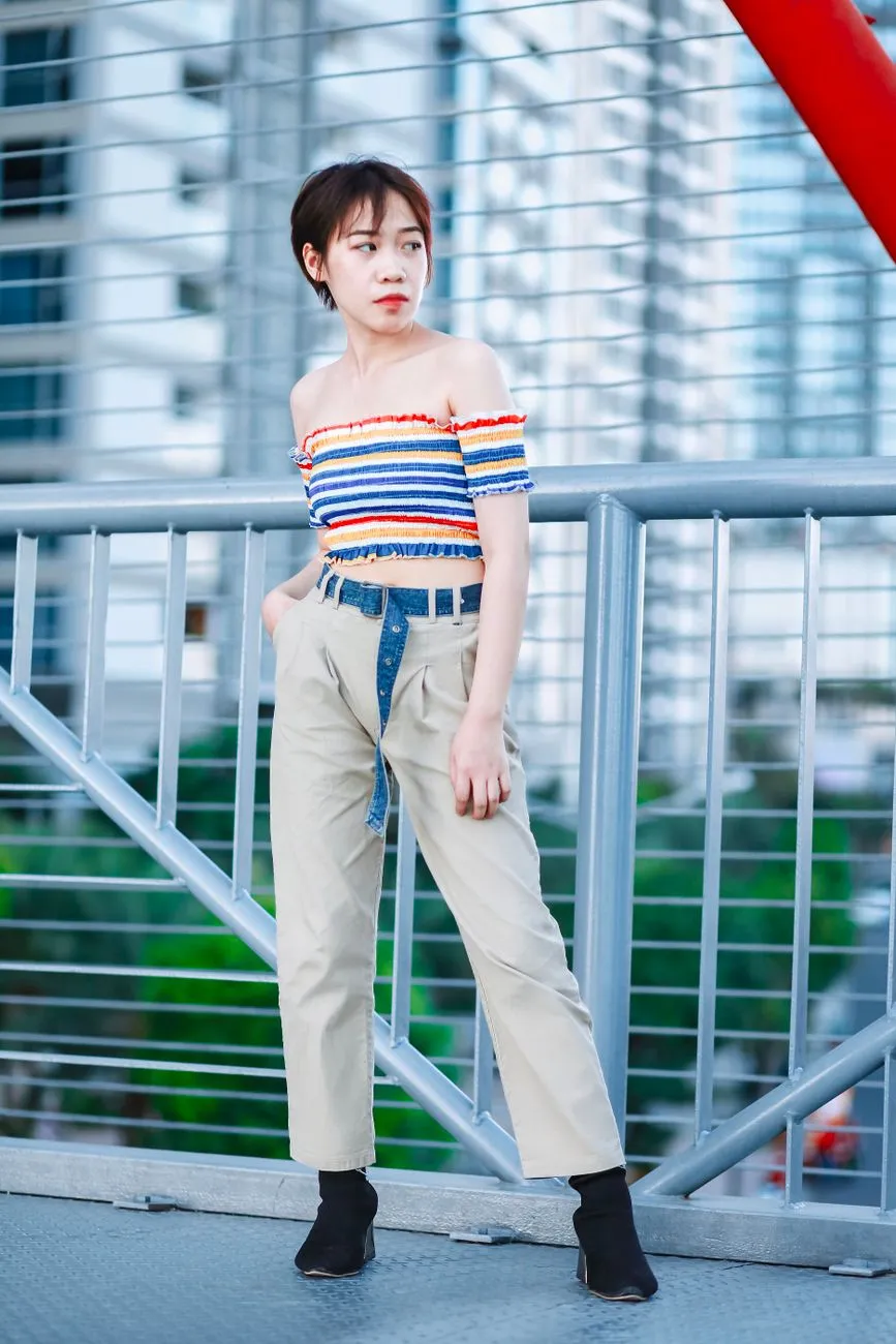 Woman in a striped off-shoulder top and high-waisted beige trousers on a city bridge
